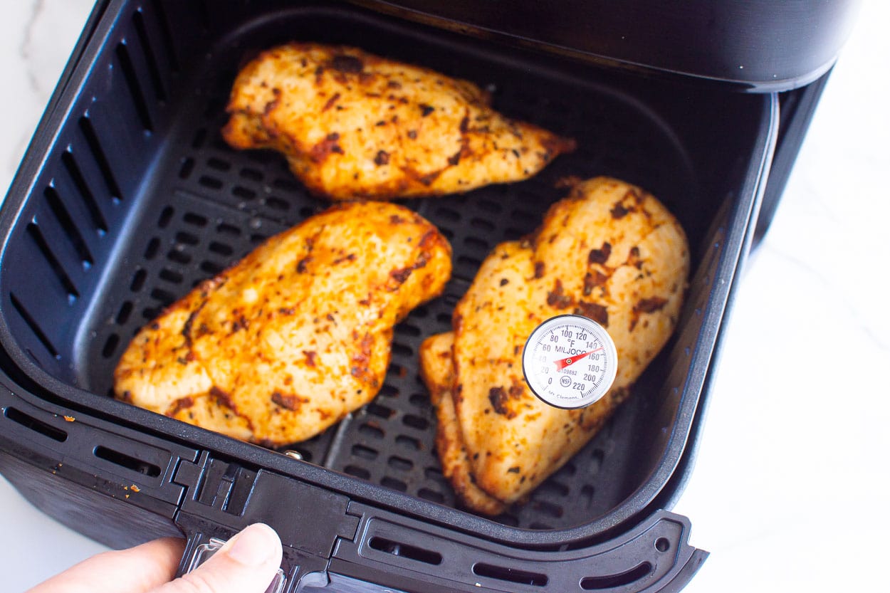 Cooked air fryer chicken breasts with thermometer inserted in one.