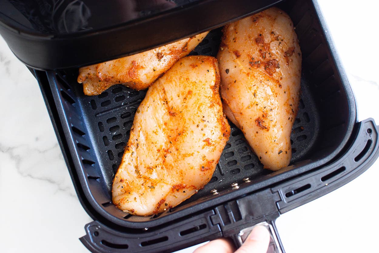 Raw seasoned chicken breasts in air fryer basket.