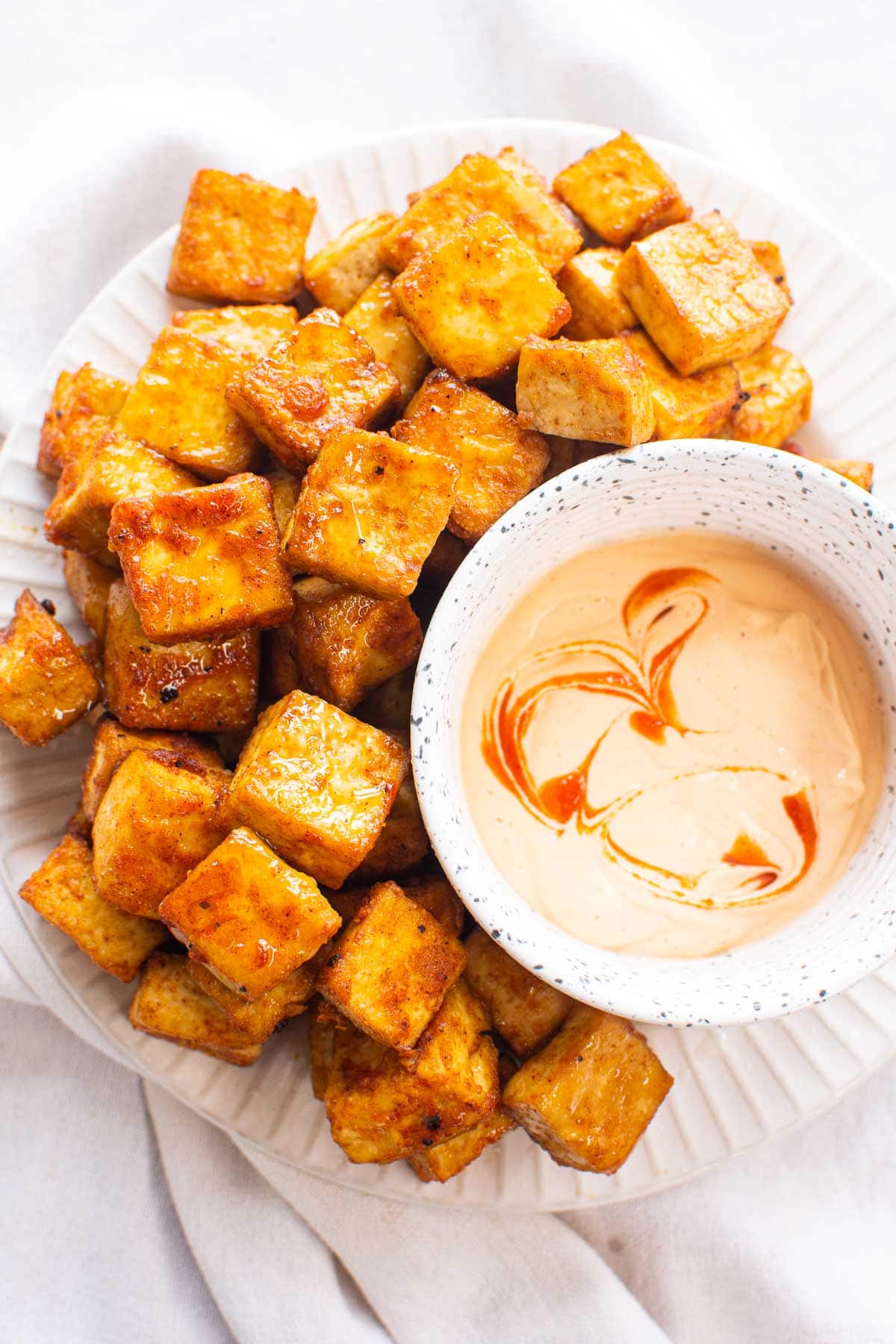 Air fryer tofu and a bowl with spicy mayo on white plate.