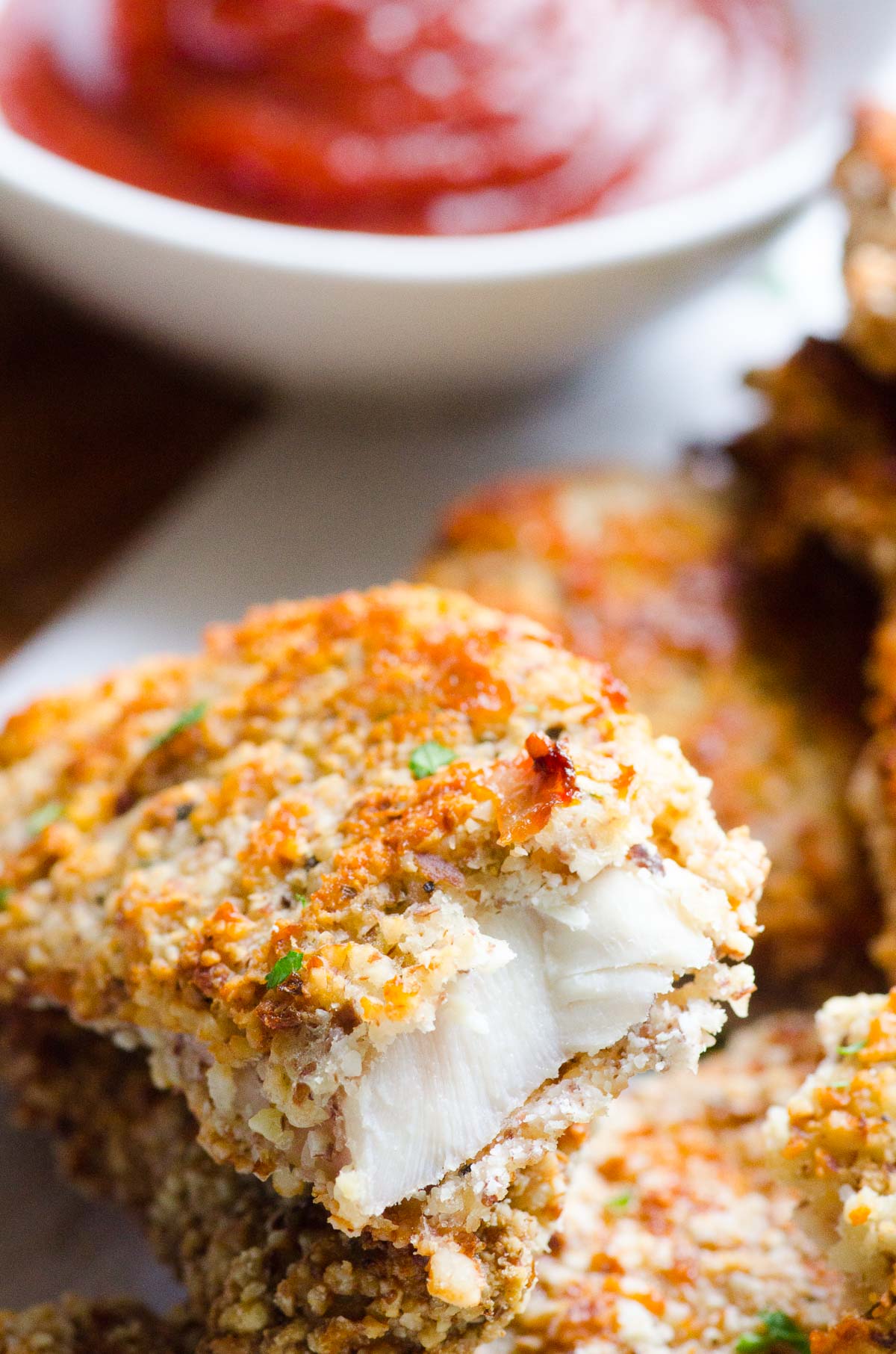 Almond crusted chicken tenders stacked on a plate with one cut open.
