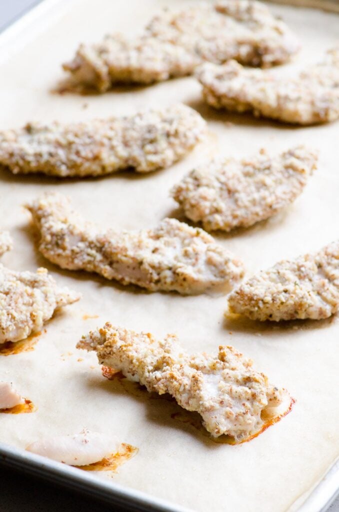 Breaded chicken tenders on parchment lined baking pan.