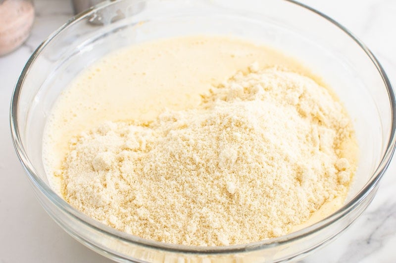 Almond flour added to wet ingredients in clear bowl.