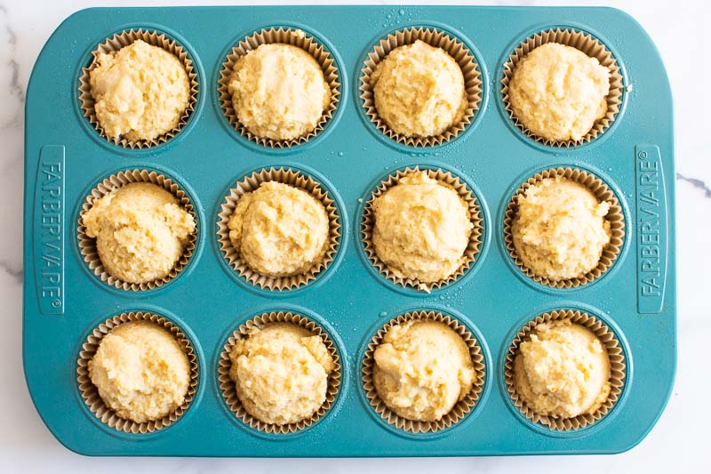 A blue muffin tin that has almond flour muffin batter inside each cavity.