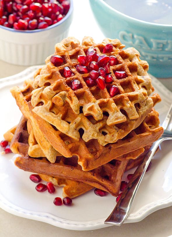 Stack of almond flour waffles on a white plate topped with pomegranate arils.