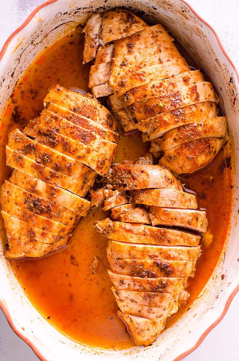 Three sliced baked chicken breasts in a baking dish.