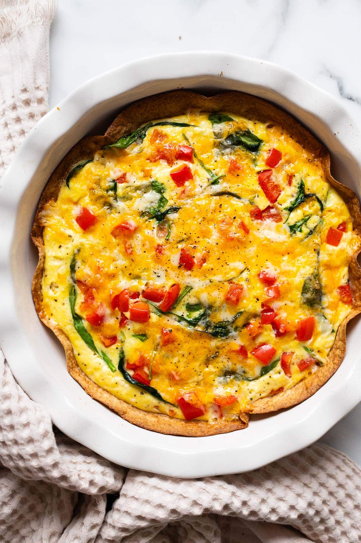 Baked egg tortilla in a baking dish with linen towel around it.