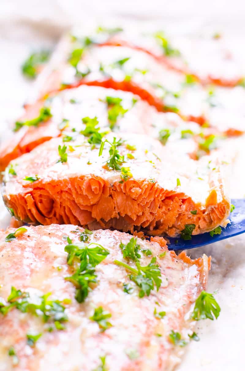 Baked salmon in foil garnished with parsley and one slice on a spatula.