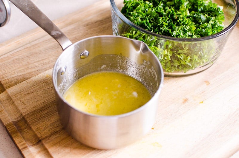 Melted butter in a pot and chopped parsley in a bowl.