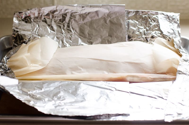 Salmon fillet wrapped in parchment paper on top of foil.