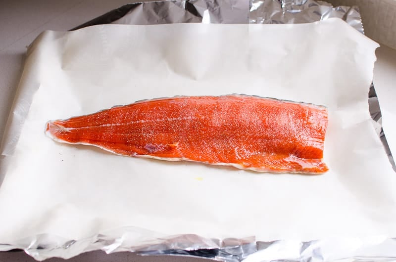Salmon fillet laying on top of parchment paper and foil.