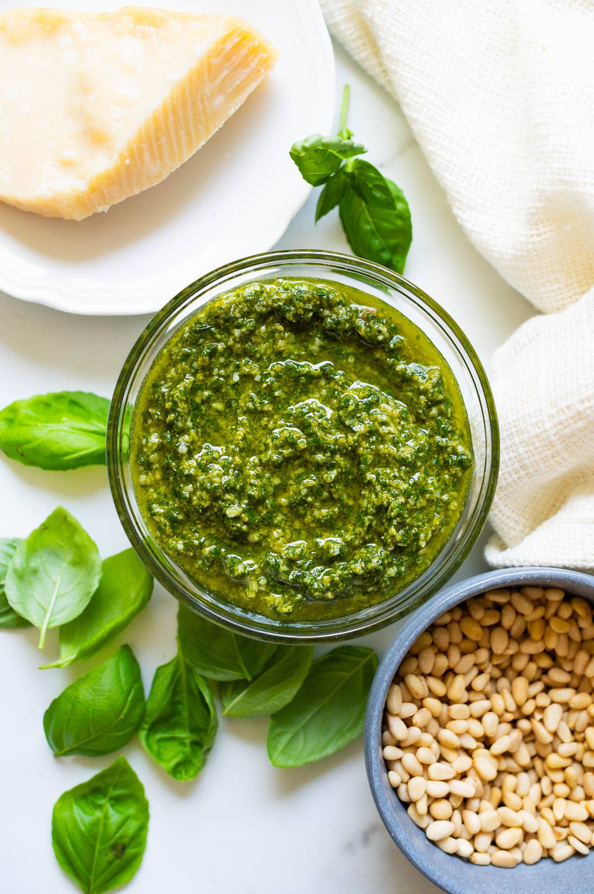 Fresh basil pesto in a glass jar. , fresh basil, parmesan cheese and napkin on the counter.