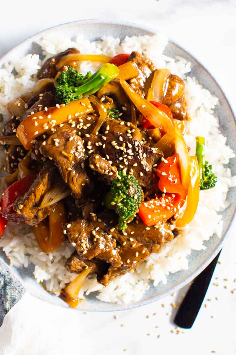 Beef stir fry served over white rice and garnish with sesame seeds.