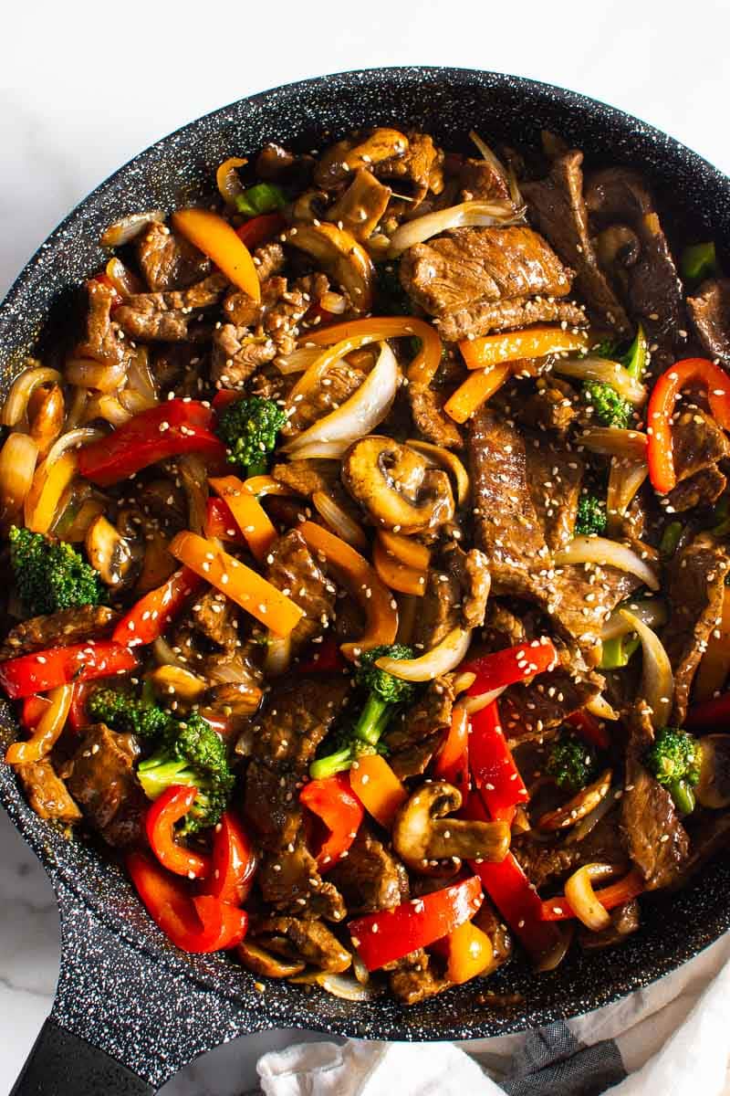 Beef stir fry garnished with sesame seeds in black skillet.