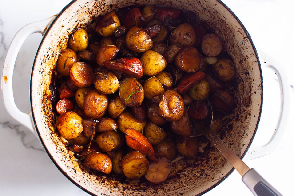 Roasted baby potatoes, carrots and mushrooms in dutch oven with metal spoon.