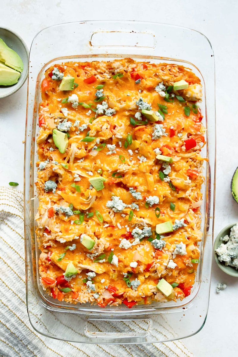 Buffalo chicken casserole garnished with blue cheese, avocado and green onion in a baking dish.