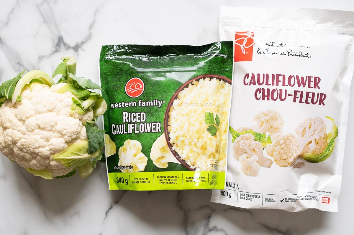Head of cauliflower, cauliflower rice and frozen cauliflower on a countertop.
