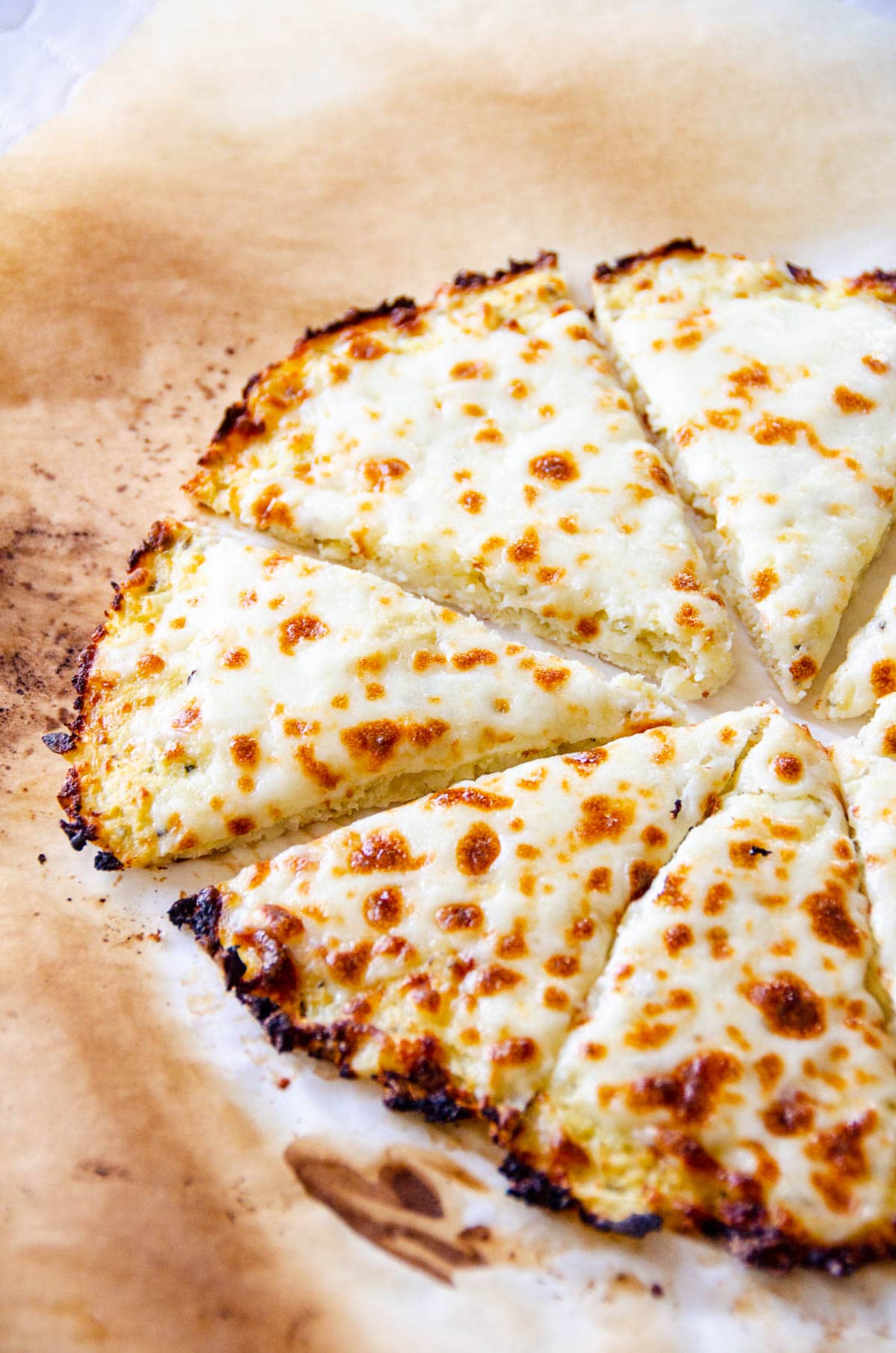 Cauliflower pizza crust with cheese on a baking sheet with parchment paper.