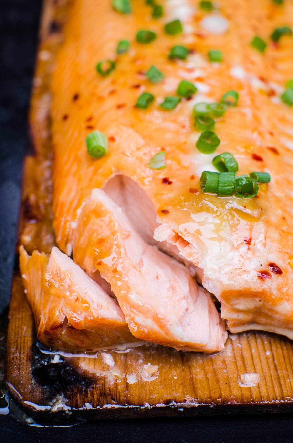 Grilled cedar plank salmon flaked with a fork and garnished with green onion.