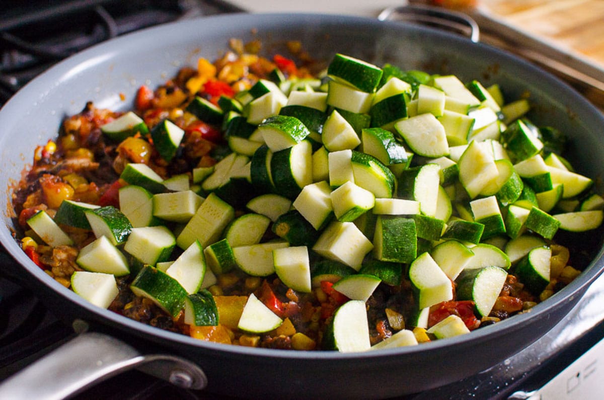 Sauteed veggies and chicken with cubed zucchini, black beans and corn piled up on top in a skillet.