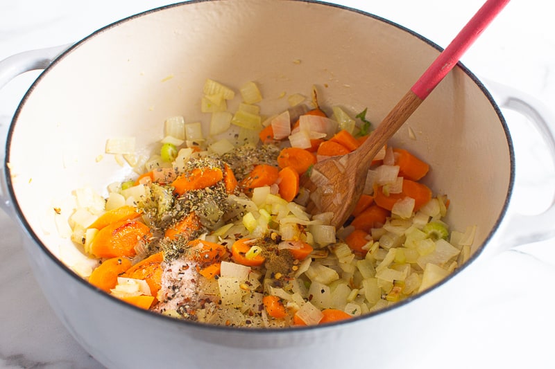 Browning onion and vegetables with herbs in a pot.