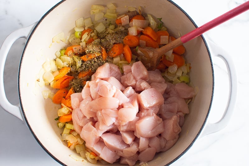 Cubed raw chicken breast with sauteed vegetables in a  with wooden spoon.