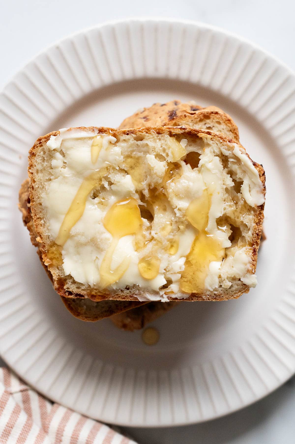 A slice of high protein cottage cheese bread with butter and honey on a plate.