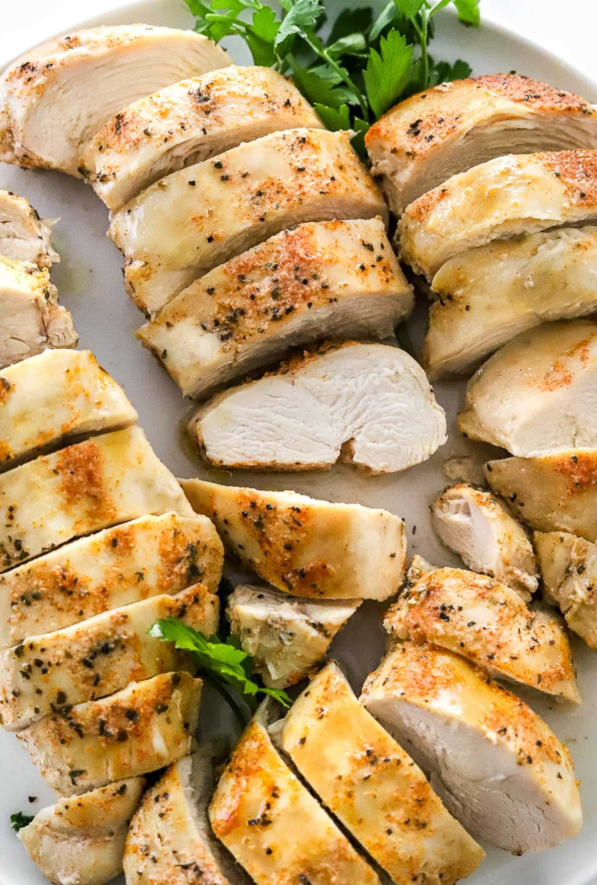 Sliced chicken breasts on a plate with parsley garnish.