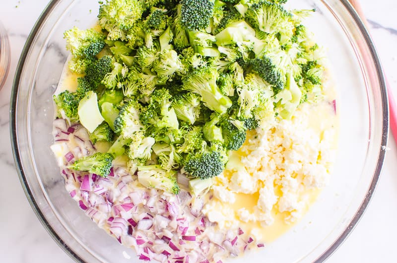 chopped broccoli, red onion and crumbled feta with egg mixture in a glass bowl