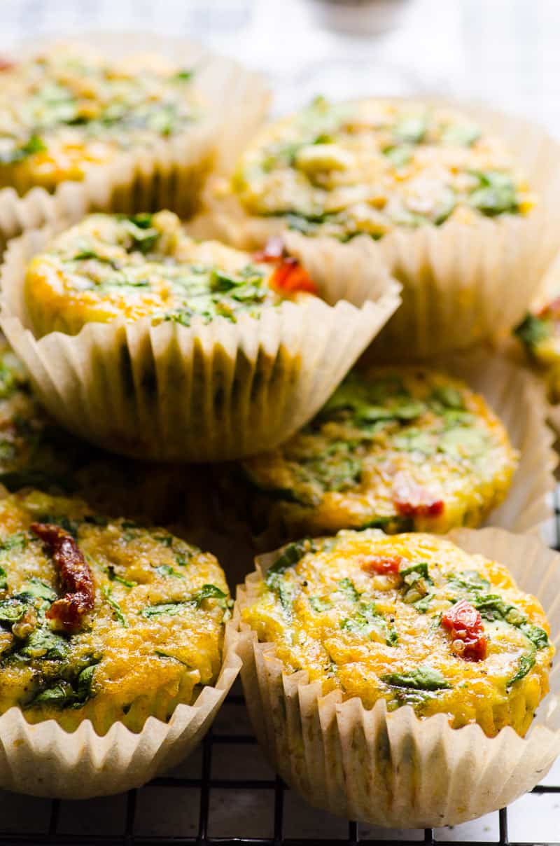 A stack of egg muffins with sun dried tomatoes and spinach in parchment paper cups.