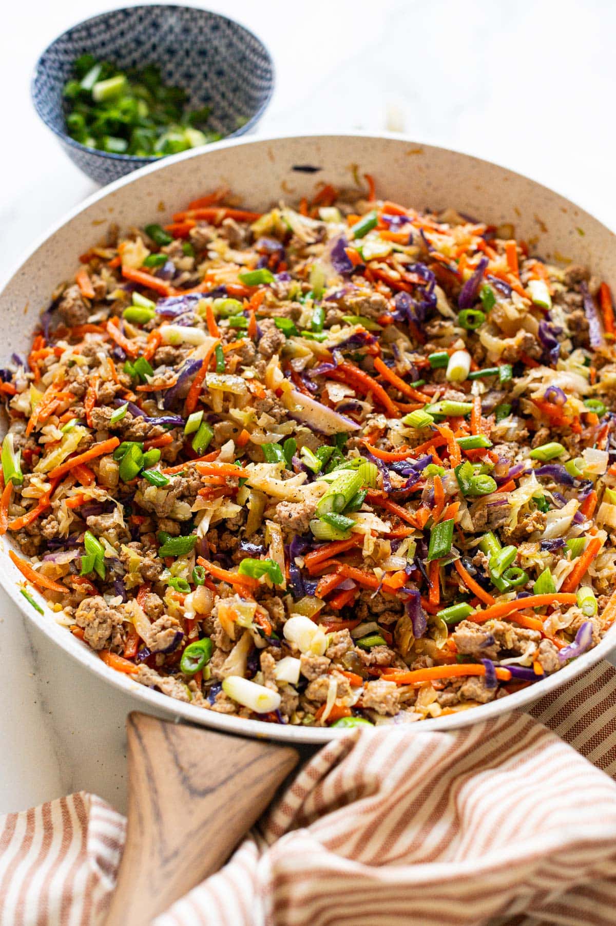 Side view of egg roll in a bowl with green onion in a skillet.