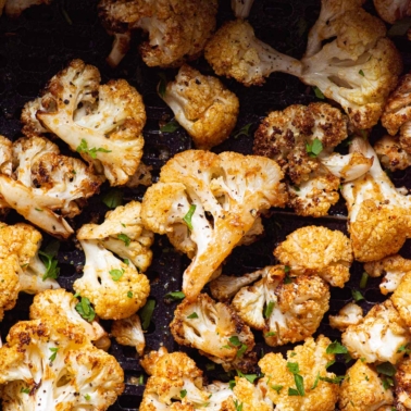 Air fryer cauliflower in the basket garnished with fresh herbs.