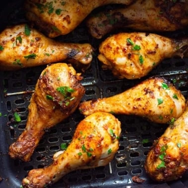 Chicken drumsticks in air fryer basket with garnish.
