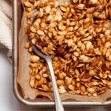 Air fryer pumpkin seeds on a baking tray scooped with a spoon.