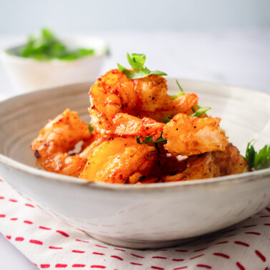 Air fryer shrimp garnished with parsley in white bowl over linen napkin.
