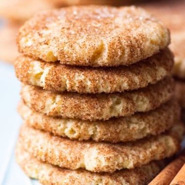 Almond flour snickerdoodles stacked on a plate with cinnamon sticks.
