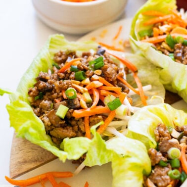 Asian turkey lettuce wraps garnished with green onion and peanuts and served on a platter.