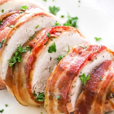 Bacon wrapped turkey breast sliced on a plate and garnished with parsley.