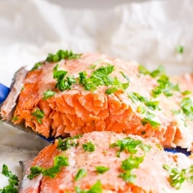 Baked salmon in foil garnished with parsley and one slice on a spatula.