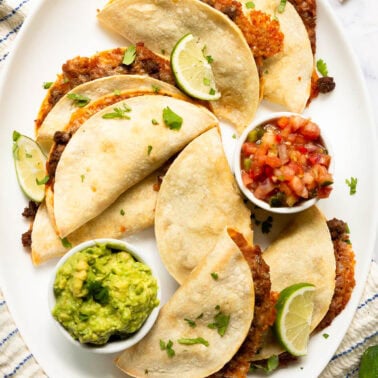 Baked tacos served with guacamole and pico de gallo on a platter.