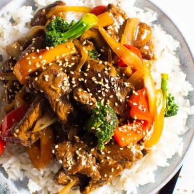 Beef stir fry served over white rice and garnish with sesame seeds.