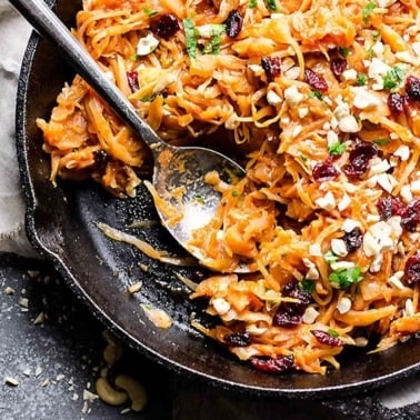 Braised green cabbage with apples topped with cashews and cranberries in cast iron skillet.