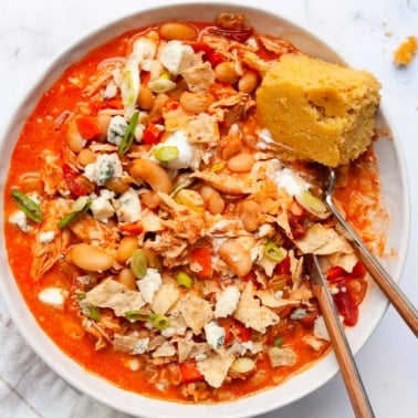Buffalo Chicken Chili in bowl with green onion, blue cheese and cornbread on a side.