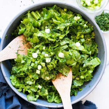 Butter lettuce salad with green onion and dill in a bowl with wooden spoons.