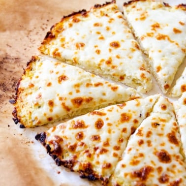 Cauliflower pizza crust with cheese sliced on parchment paper.