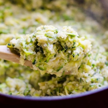 Cheesy cauliflower rice with zucchini on a wooden spoon.