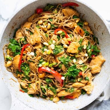 Chicken soba noodles stir fry garnished with peanuts and green onion in a skillet.