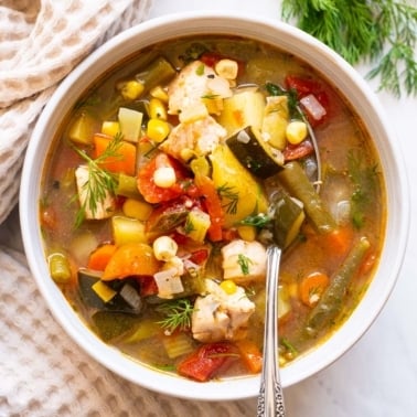 Chicken vegetable soup in a bowl with a spoon.