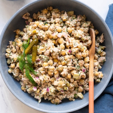 Chickpea tuna salad in a bowl with wooden spoon and topped with fresh dill and pickles.