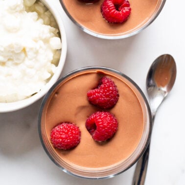 Cottage cheese chocolate pudding garnished with raspberries in small cups with spoons.