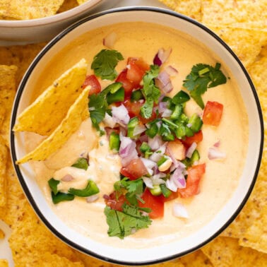 Cottage cheese queso dip with tomatoes, red onion, jalapeno and cilantro in a bowl with tortilla chips.